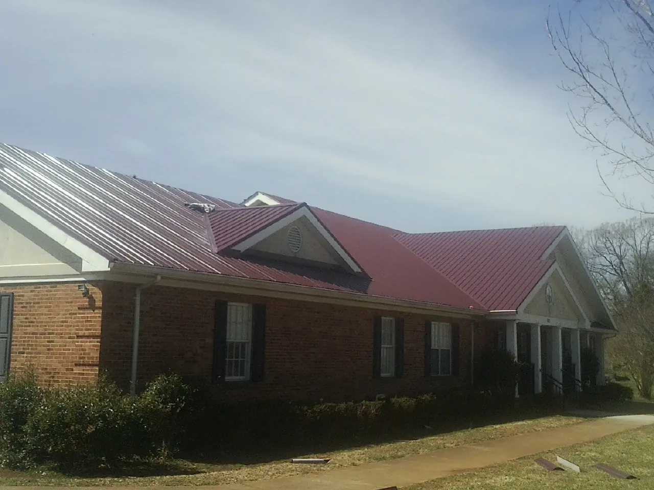 Red metal roof with gabled entries on a long brick building, from a Hail Damage Roof Repair job in Detroit Lakes