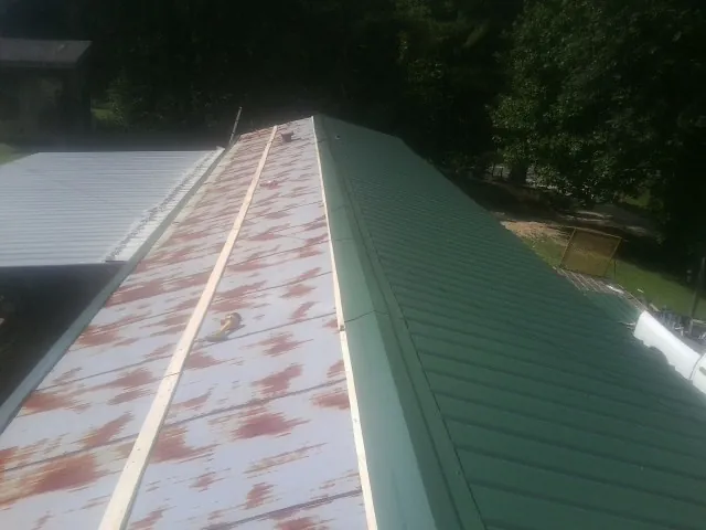 Old rusted panels beside newly installed green metal roofing — Wind Damage Roof Repair by Roofing Brothers in Detroit Lakes
