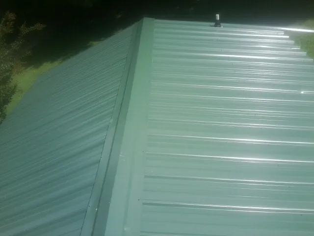 New green metal panels meeting at the ridge of a roof — Flat Roof Repair work by our crew in Detroit Lakes