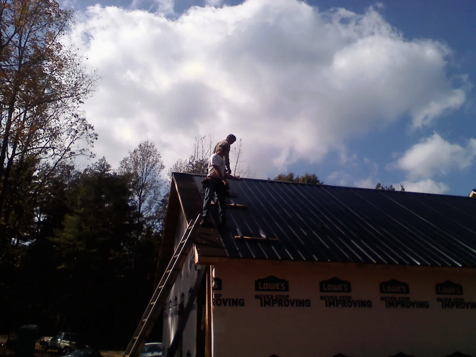 Roofer fastening dark metal panels high against a cloudy sky, from a Roof Inspection job in Detroit Lakes