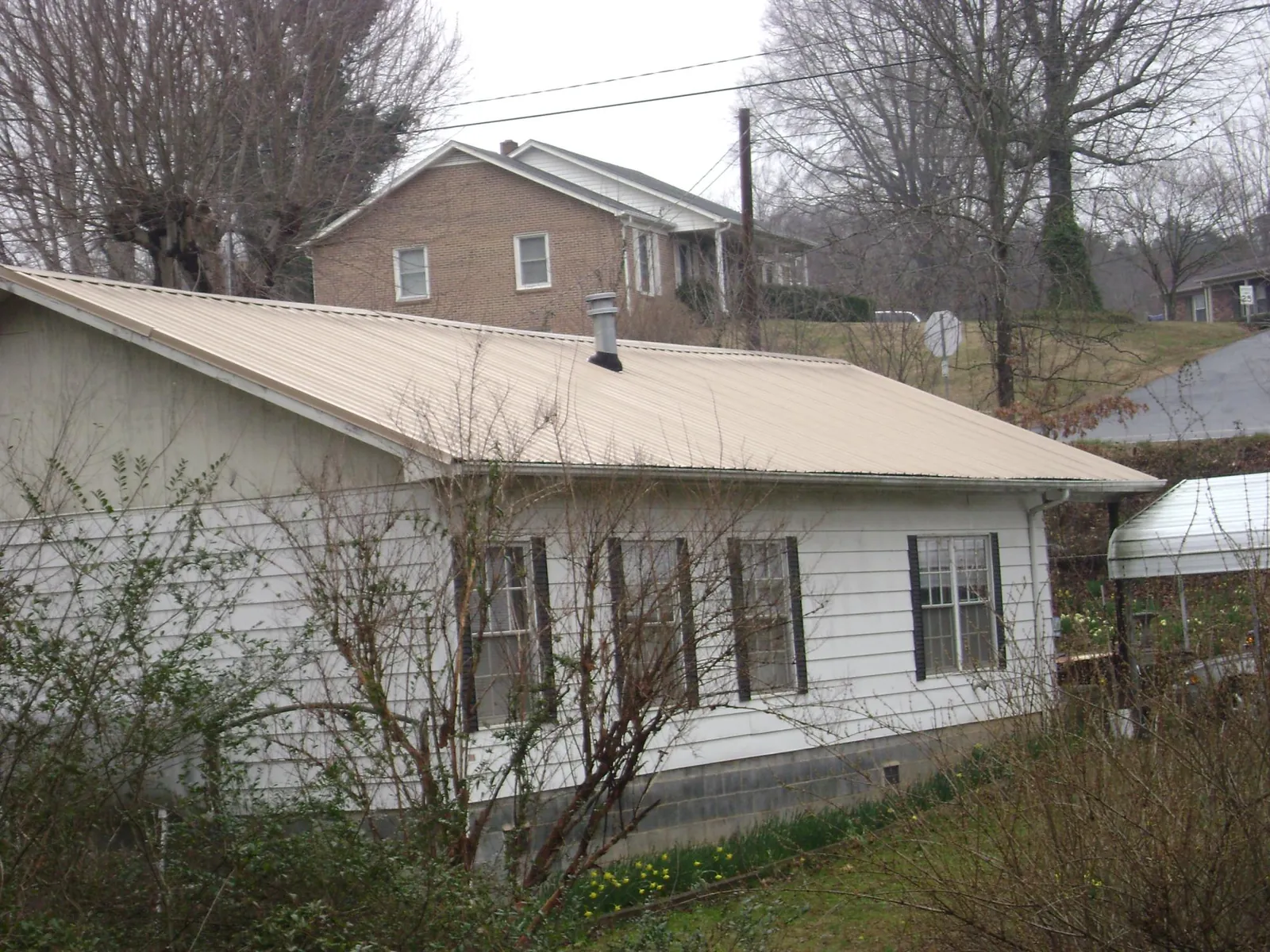Tan metal roof on a white sided house set into a hillside — Commercial Roofing by Roofing Brothers in Detroit Lakes
