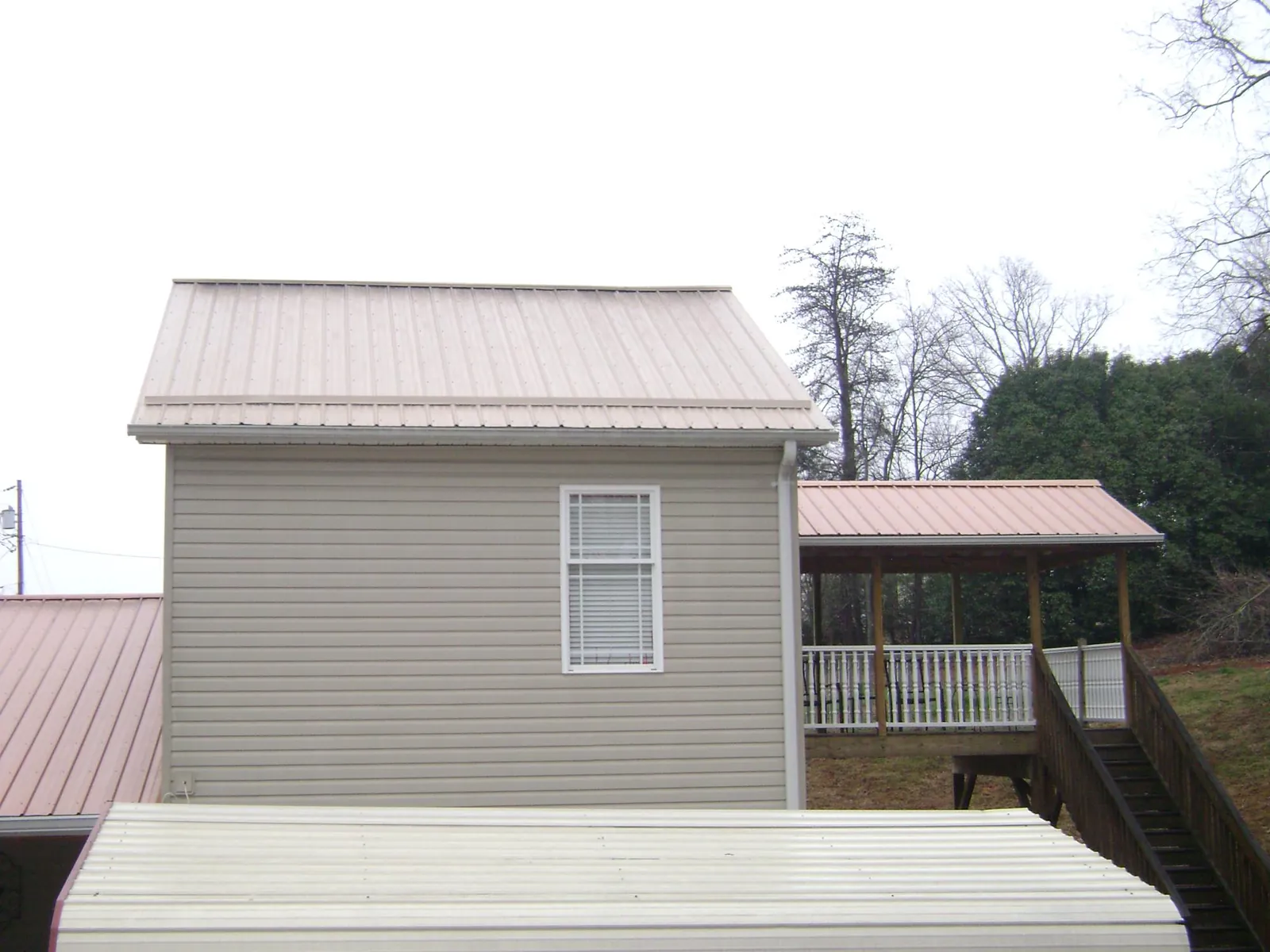 Tan metal roofs on a two story addition and attached porch, from a Roof Replacement job in Detroit Lakes